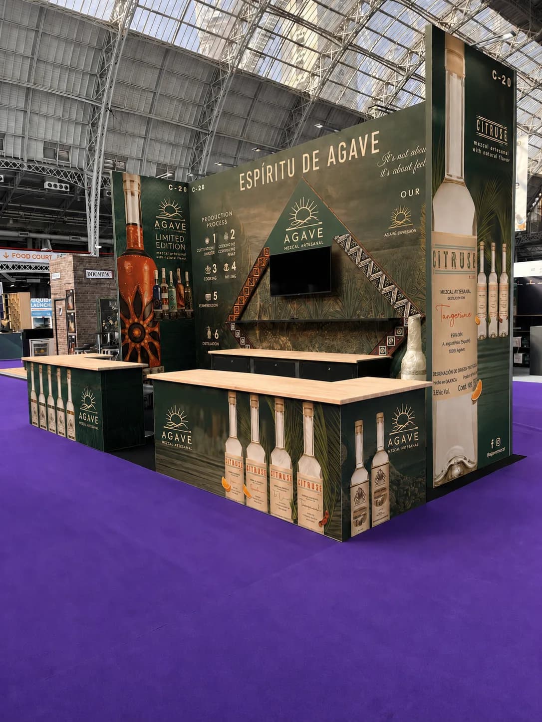 Agave mezcal exhibition stand with dark green graphics, timber counters, bottle motifs and an integrated screen