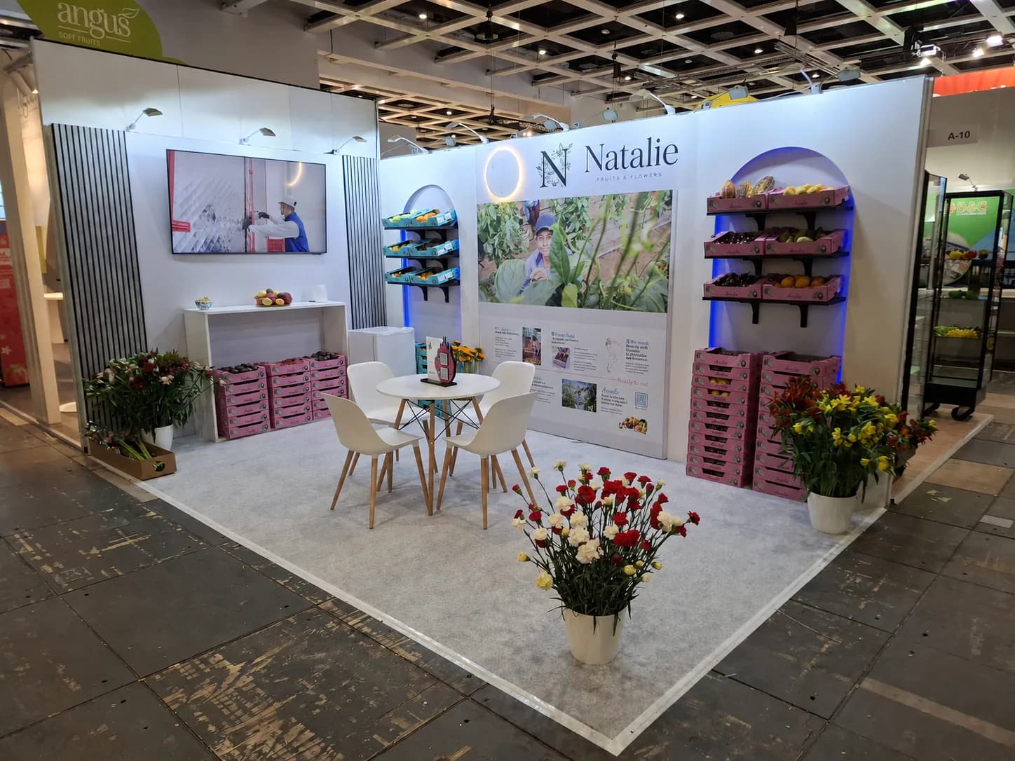 Fruit and flower exhibition stand with illuminated product shelving, a screen and seating area